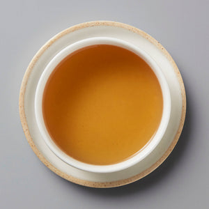 MADE-FOR-TV sheng puer tea served in white ceramic cup, showing amber-colored liquor on grey background