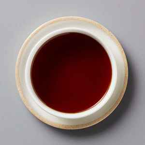 2023 DIGESTIF shou puer tea in white ceramic cup with rich dark red liquor against grey background