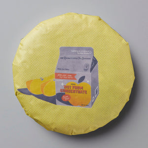 2023 Not From Concentrate white tea cake with illustration of oranges and milk carton on yellow circular wrapper