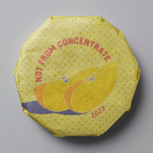 2023 Not From Concentrate white tea cake with yellow wrapper featuring stylized citrus fruit design in orange and yellow