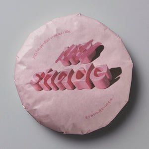 2023 NO SHADE white tea cake in pink wrapper with 3D lettering on circular compressed tea disc