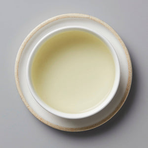 Session Longjing green tea in a white ceramic cup showing pale yellow-green liquor against grey background