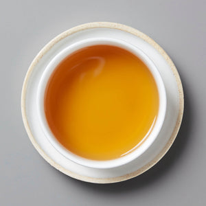 Anshun Jin Jun Mei black tea with golden amber liquor in traditional white ceramic cup, viewed from above