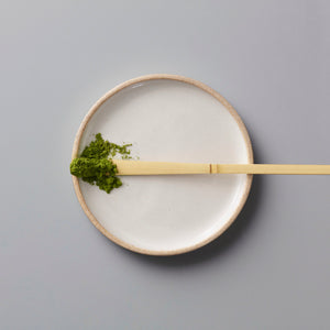 Ceremonial grade MATCHA ANSHUN vibrant green powder on bamboo scoop, placed on minimalist ceramic plate.