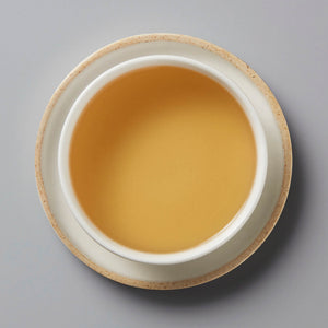 Grandpas Pocket huangpian sheng puer tea in white ceramic cup showing golden amber colored liquid on gray background