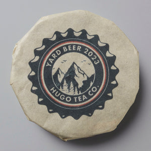 Yard Beer 2023 tea cake with Hugo Tea Co logo featuring mountains and bottle cap design on wrapped packaging