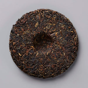 2020 BRUISER black tea cake, compressed dark leaves in traditional circular disc shape against grey background