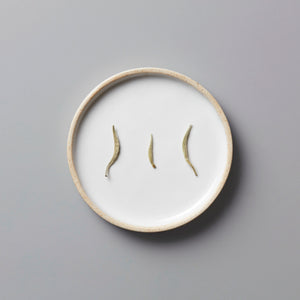 Ma Wei Needles white tea buds displayed on white ceramic plate with beige rim against grey background