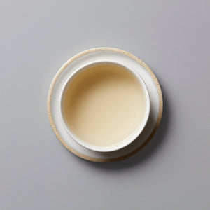 Ma Wei Needles white tea in ceramic cup showing pale golden liquor against grey background