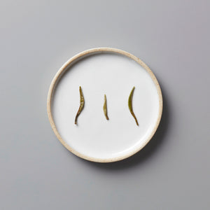 Ma Wei Needles white tea buds displayed on white ceramic plate showing three delicate silver needle tea leaves