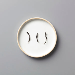 Three twisted Panlan Que She yancha oolong tea leaves arranged on a minimalist white ceramic plate