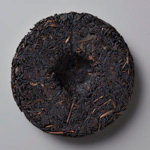 Smoke Break black tea cake, compressed dark leaves with rustic texture against grey background