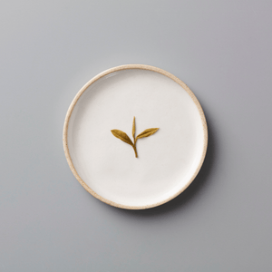 YINYU ANJI BAICHA green tea leaves displayed on a white ceramic plate with beige rim against grey background