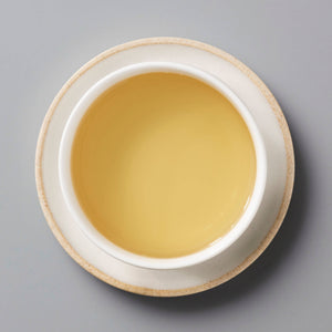 Fuding Bai Mudan white tea in a ceramic cup showing golden amber liquor against grey background