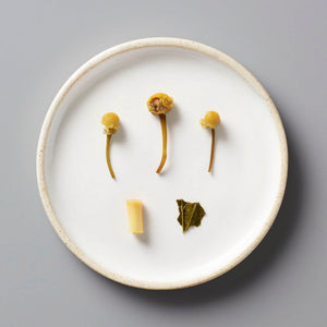 BOUQUET tisane blend ingredients displayed on white ceramic plate featuring dried chamomile flowers, lemongrass, and mint leaf