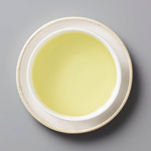 CHRYS tisane in white ceramic cup showing pale yellow chrysanthemum tea liquor against grey background