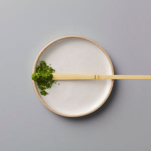 Matcha Scoop Chashaku bamboo tea scoop with green matcha powder on white ceramic plate against grey background