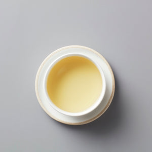 Long Kou Maofeng green tea in white ceramic cup showing pale yellow-green liquor against grey background