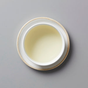 Popped Genmai tisane served in white ceramic cup with pale yellow liquid, viewed from above on grey background