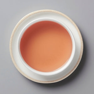 ROSE tisane steeped to a vibrant pink color in white ceramic cup, top-down view on grey background