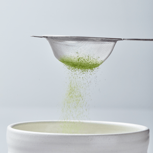 Matcha Sifter sieving bright green tea powder into white ceramic bowl against light gray background