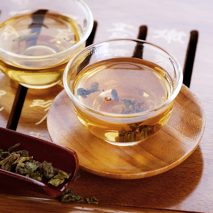 Brewed oolong tea in glass cups with rolled oolong leaves nearby.