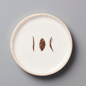 Three wet bai mu dan leaves on a white ceramic plate with a beige rim against a gray background