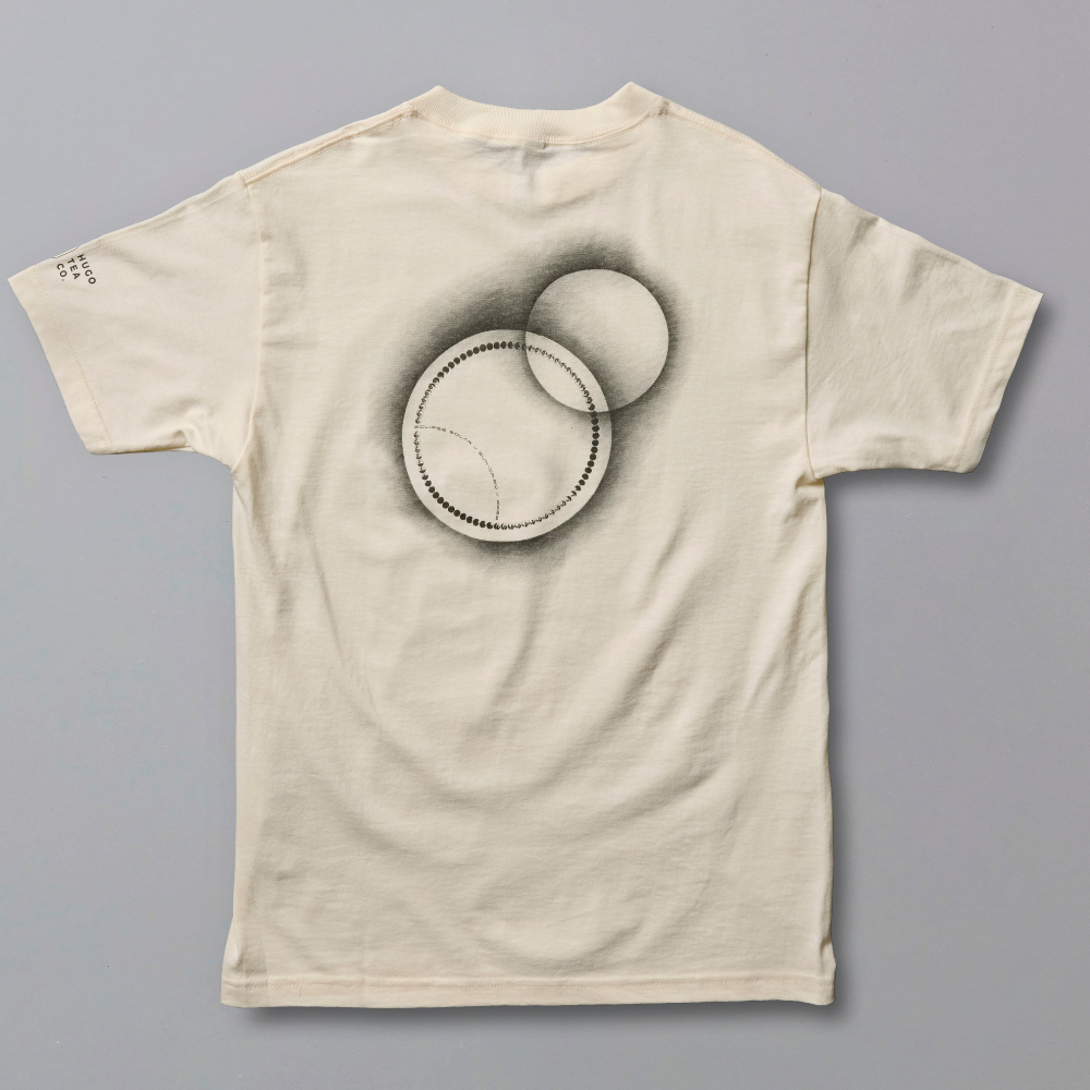An off-white short-sleeve t-shirt with a black and gray graphic of overlapping circles on the front, laid flat against a solid gray background.