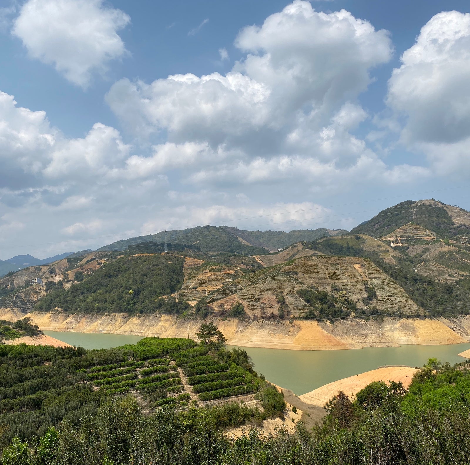 Scenic view of a lush green valley with terraced fields, a calm river, and distant mountains under a partly cloudy sky. A serene and peaceful landscape.