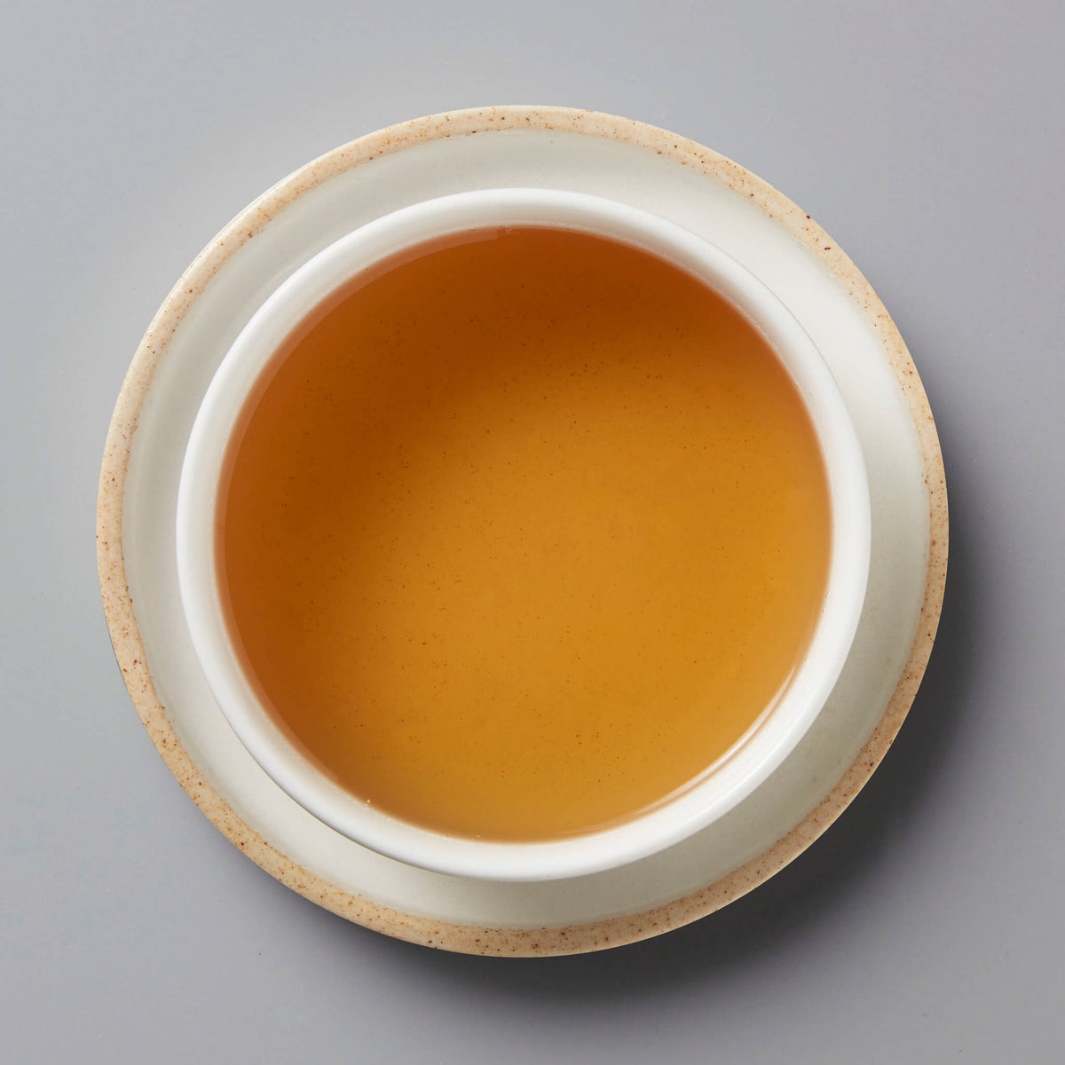 MADE-FOR-TV sheng puer tea served in white ceramic cup, showing amber-colored liquor on grey background