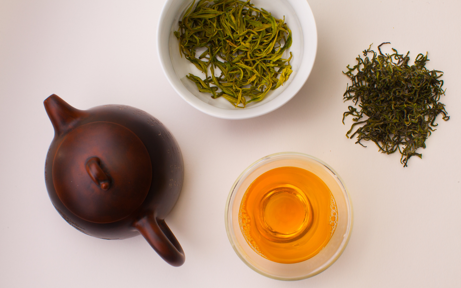 Tea-making setup with teapot, dried tea leaves, and brewed tea in a glass cup.