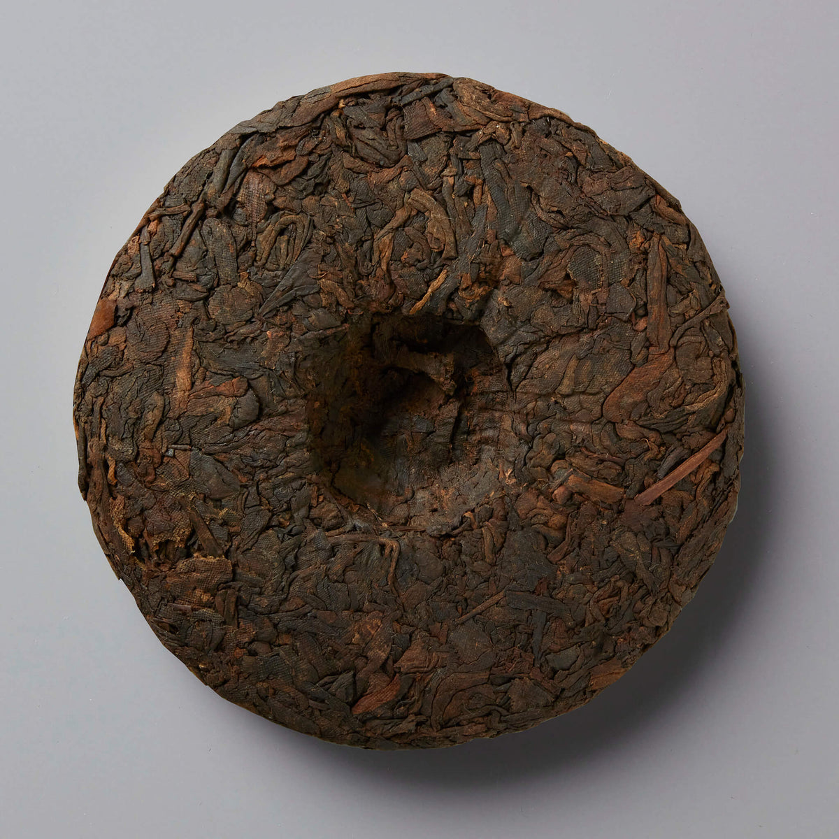 2023 DIGESTIF shou puer tea cake with dark compressed leaves and center depression on grey background