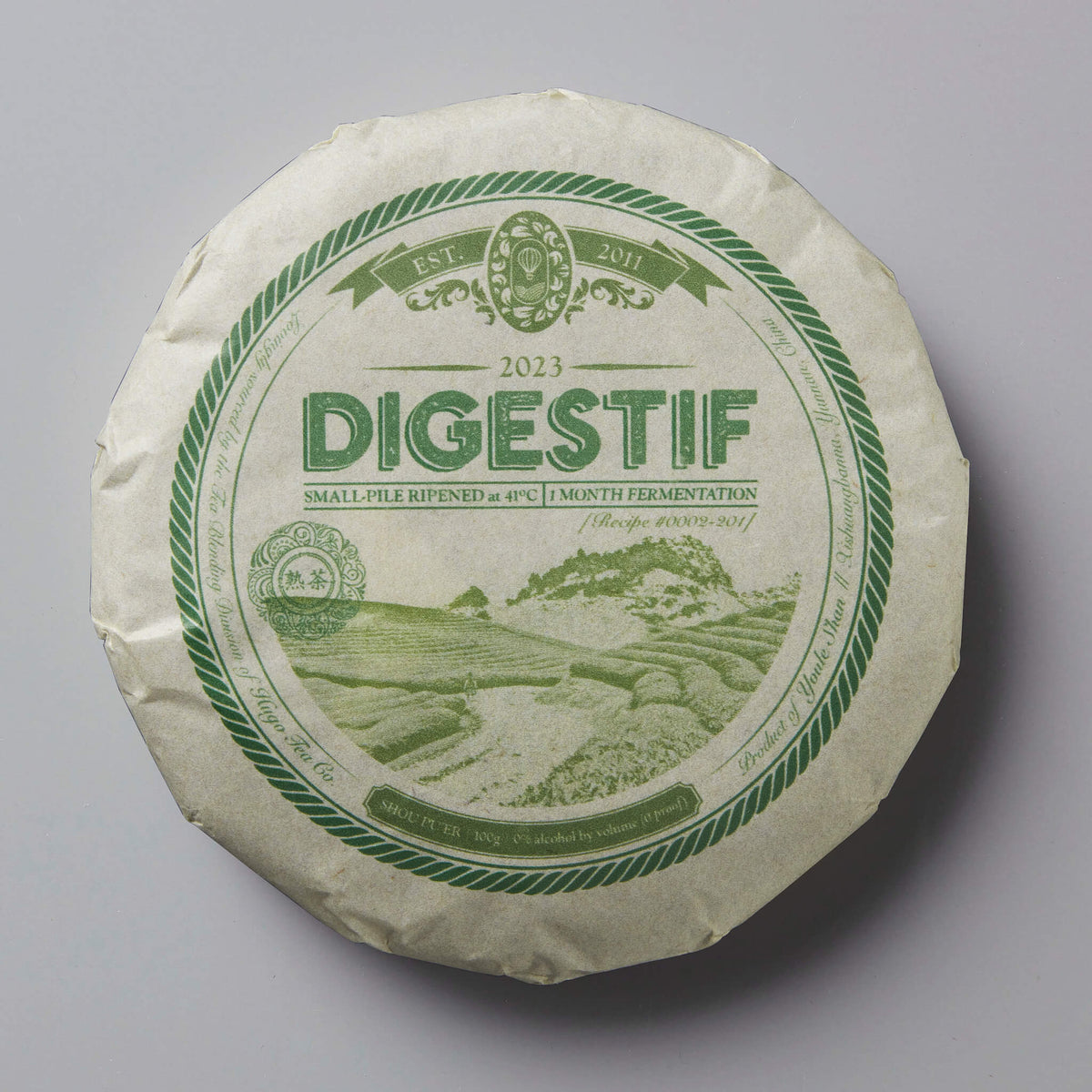 2023 Digestif shou puer tea cake with green circular label showing mountain landscape and rope border design