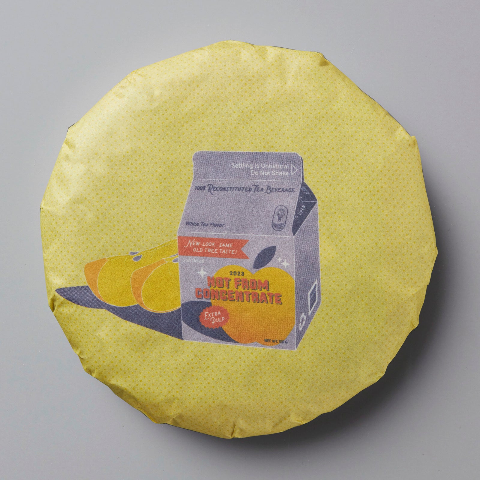 2023 Not From Concentrate white tea cake with illustration of oranges and milk carton on yellow circular wrapper