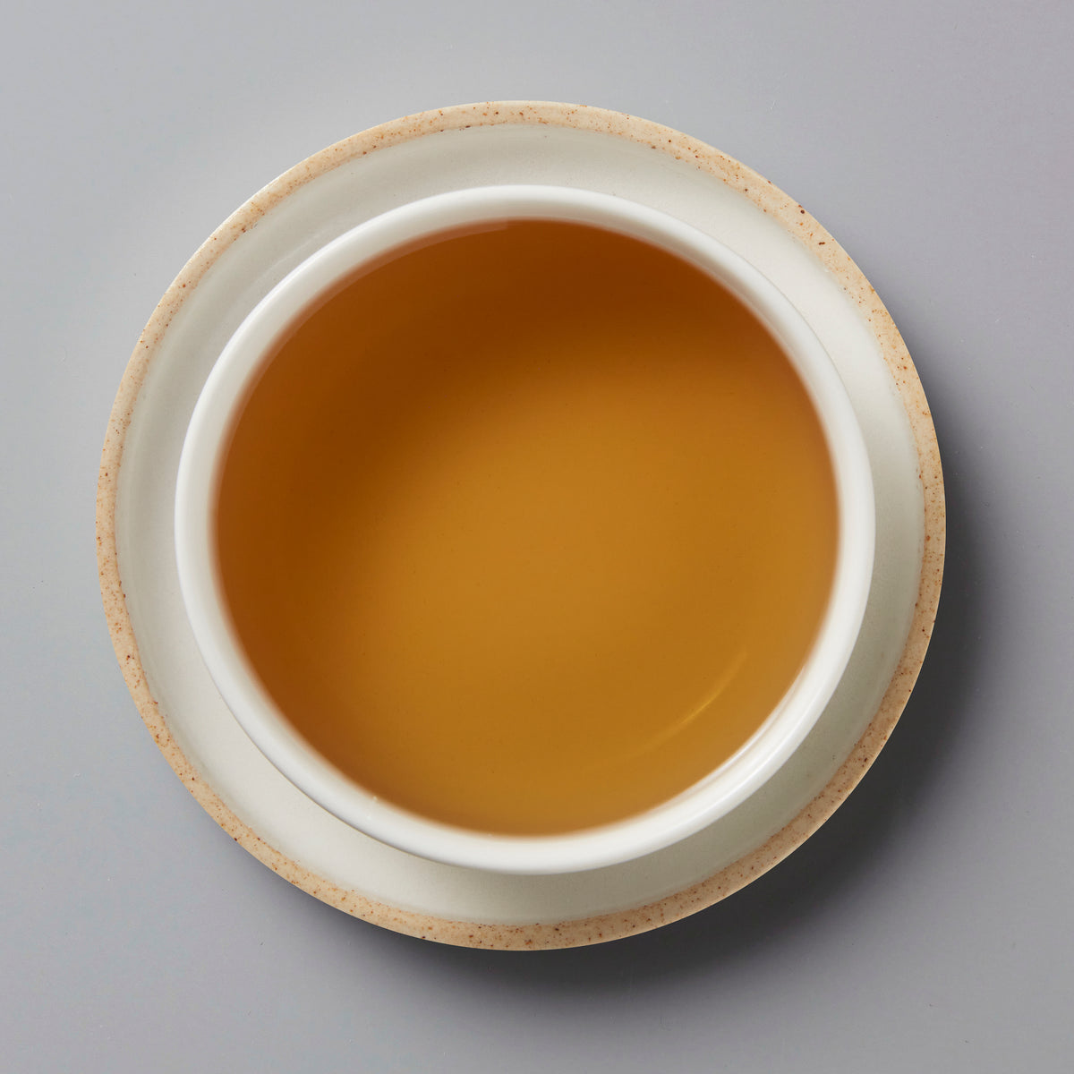 Cup of amber-colored NO SHADE white tea in ceramic vessel viewed from above on grey background