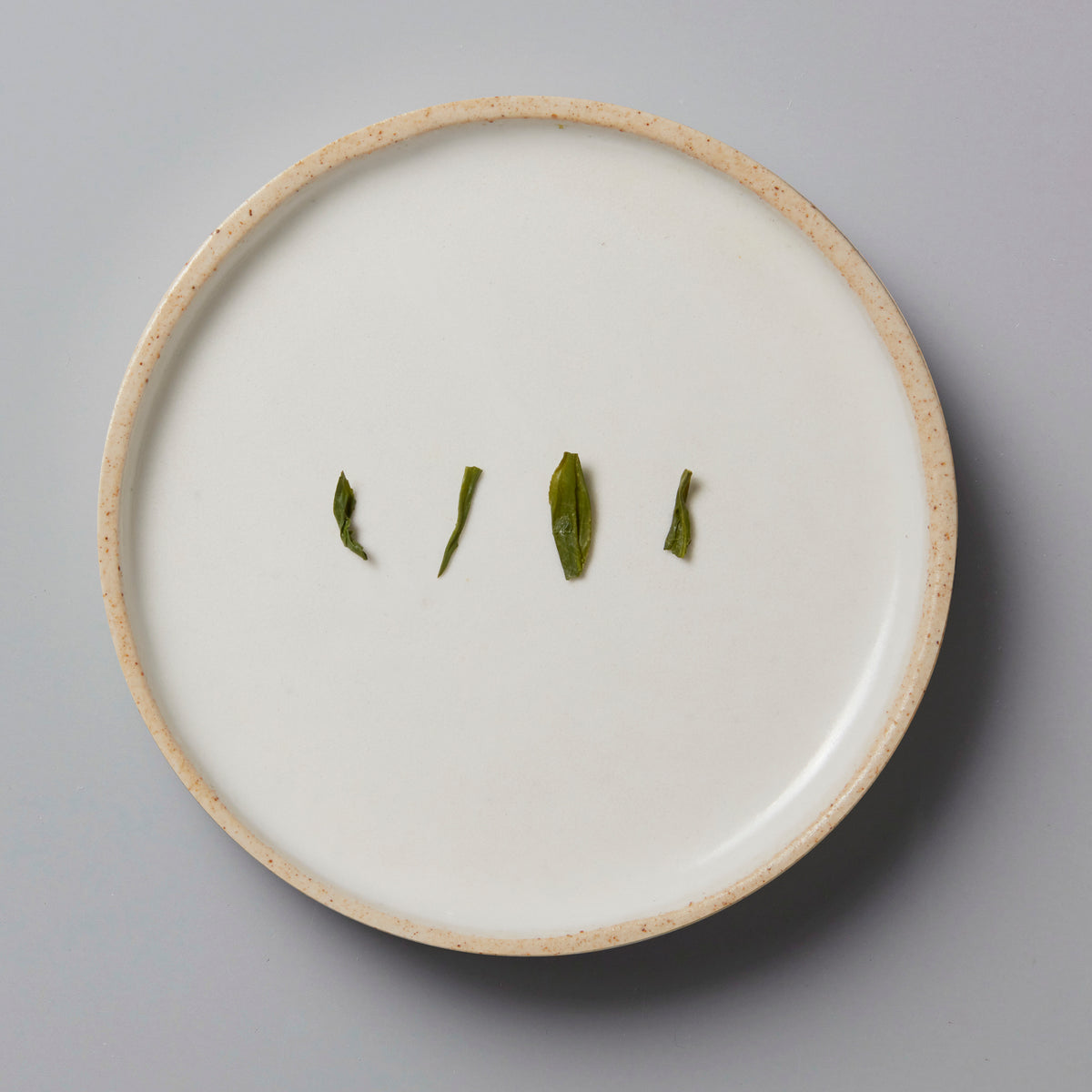 Sonogi Tama green tea leaves arranged on white ceramic plate showing different cultivar leaf shapes and textures