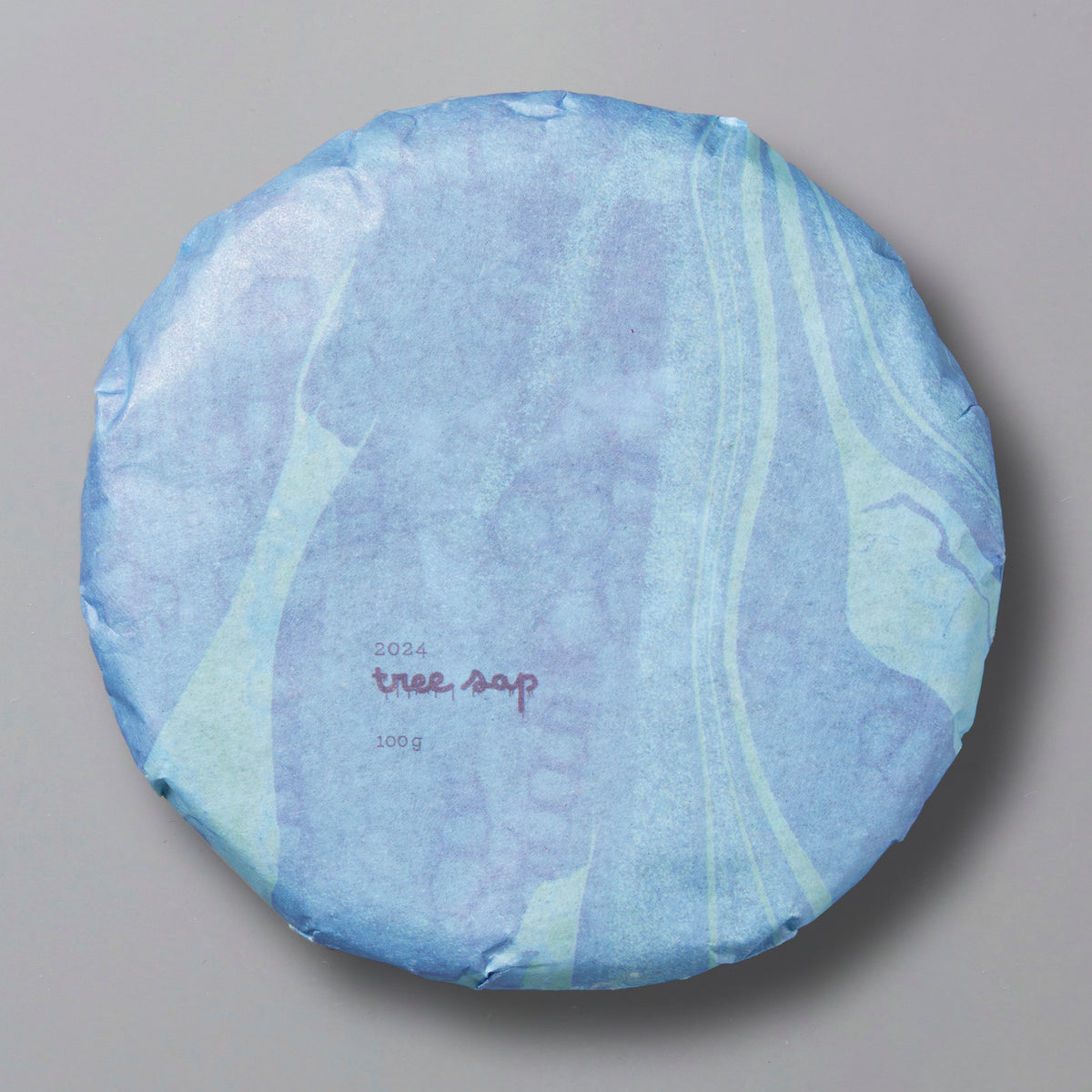 A packaged round tea cake labeled 'Tree Sap 2024' in blue and white design, indicating it is a black tea from Lincang, Yunnan.