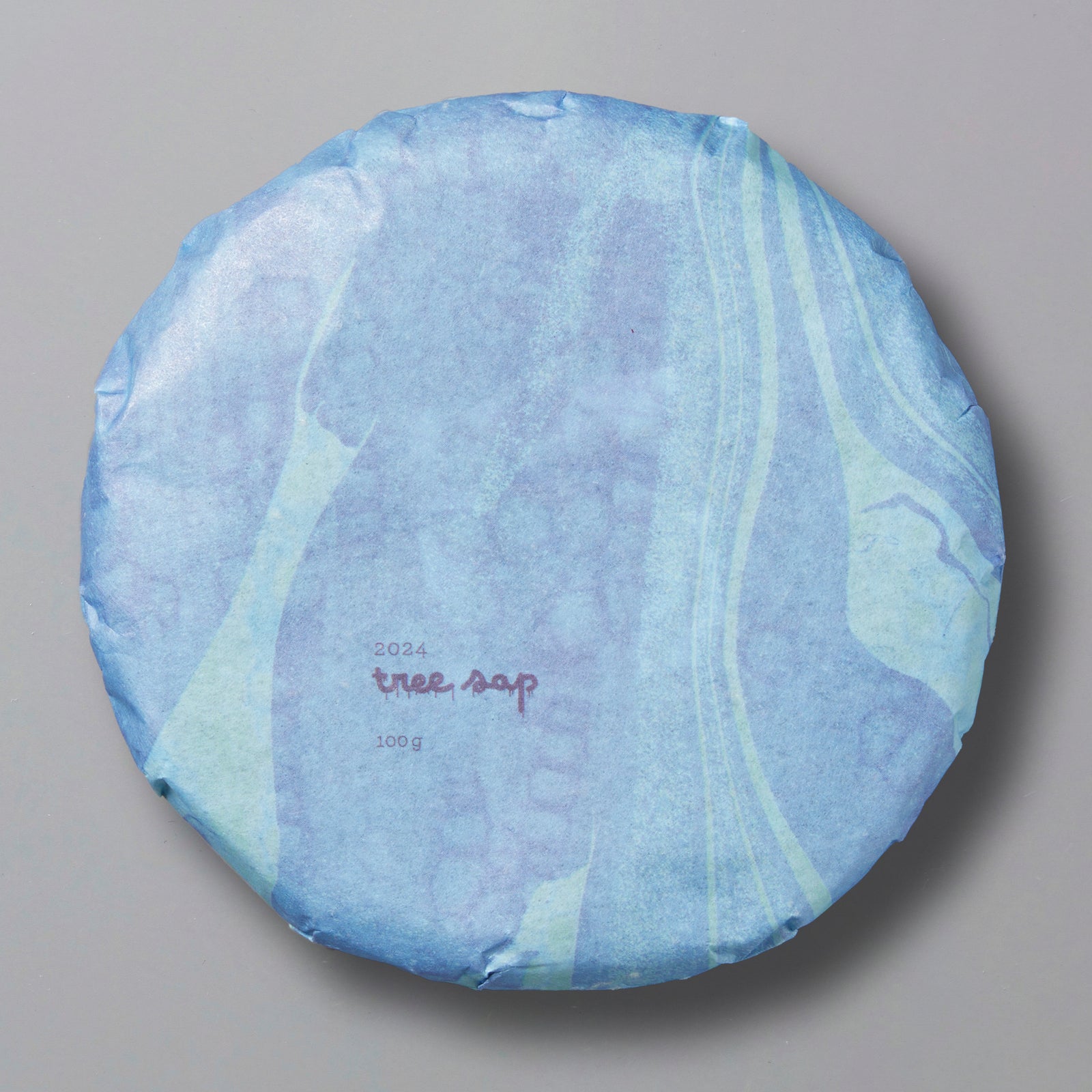 A packaged round tea cake labeled 'Tree Sap 2024' in blue and white design, indicating it is a black tea from Lincang, Yunnan.