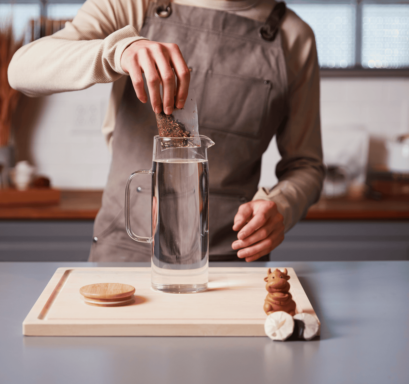 Person in a kitchen adding a tea bag into a glass pitcher filled with water.
