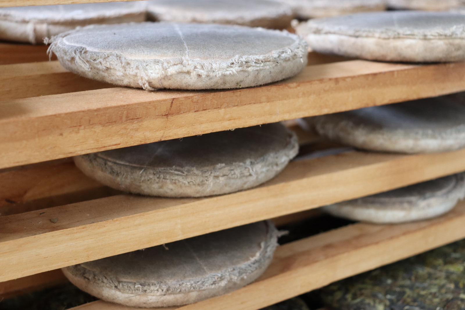 Close-up of round tea cakes enveloped in cloth, aging on stacked wooden shelves. The setting appears rustic, conveying a sense of tradition and craftsmanship.