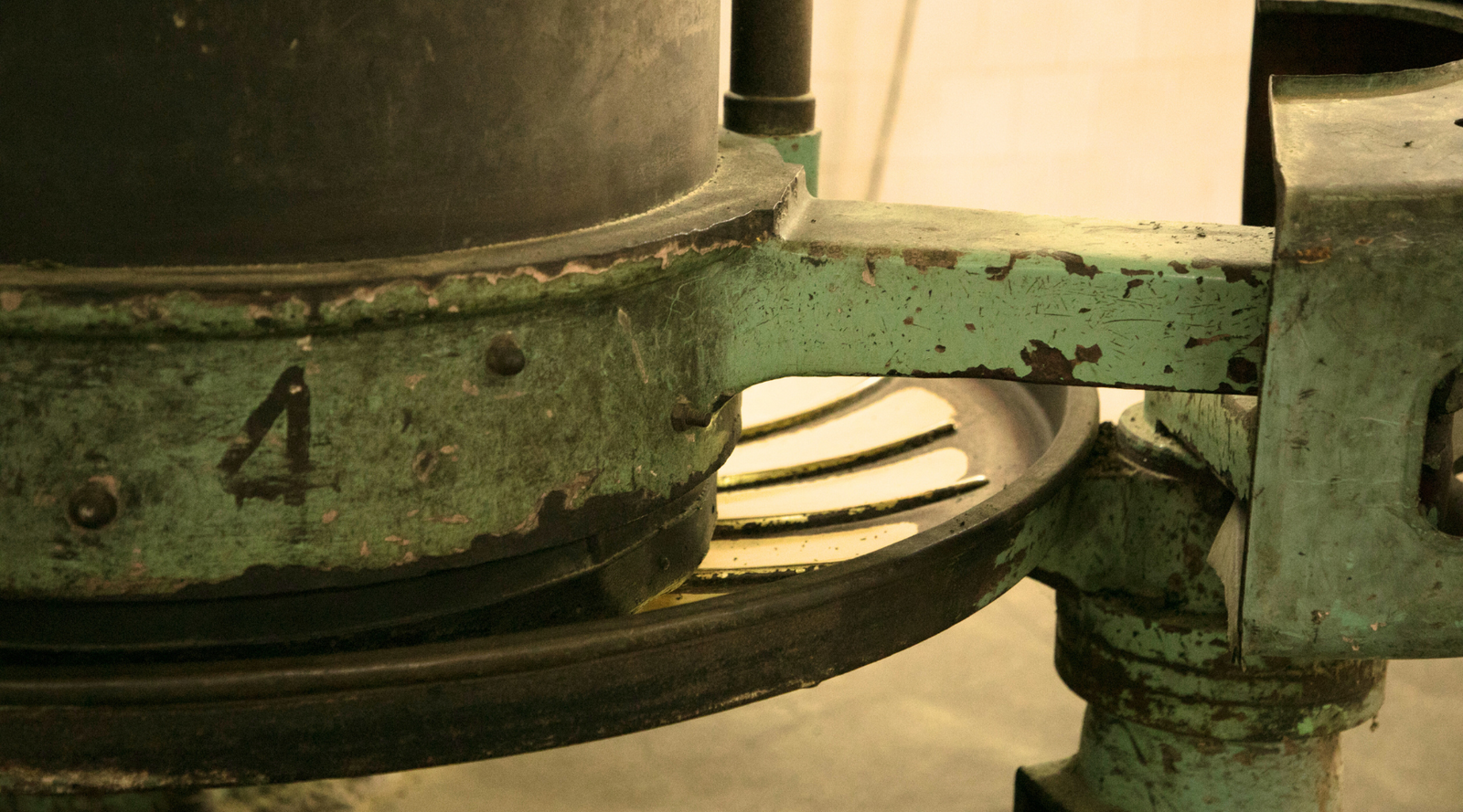 Close-up of an old, weathered industrial machine with a faded green surface and large black cylinder. The number "4" is visible, conveying an antique, rustic feel.