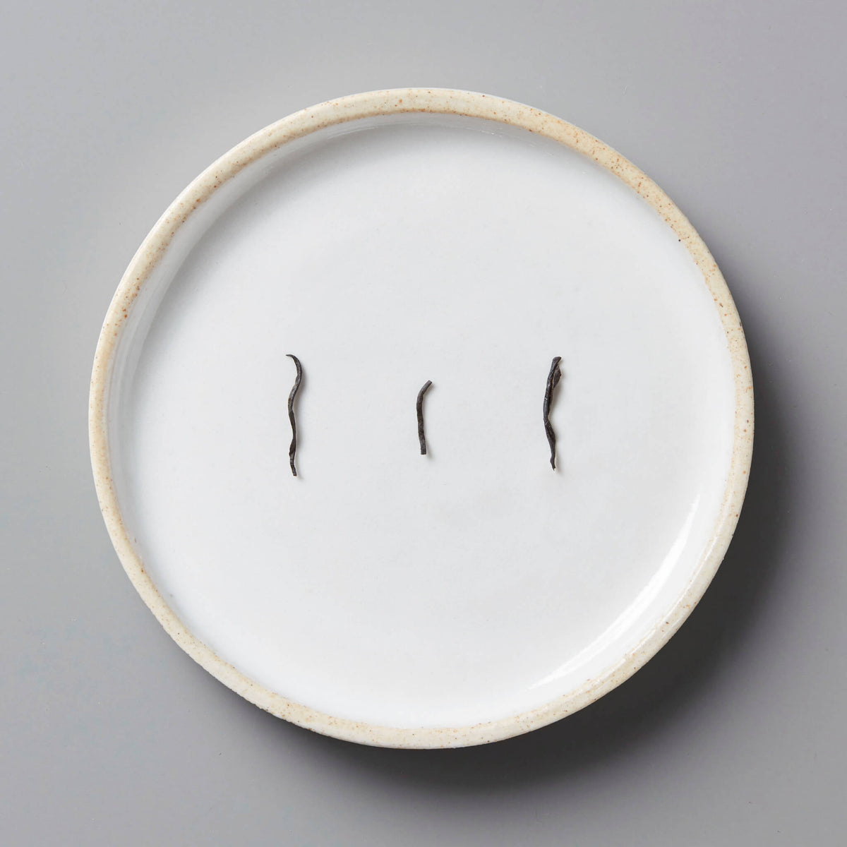 Anshun Jin Jun Mei black tea buds displayed on white ceramic plate with beige rim