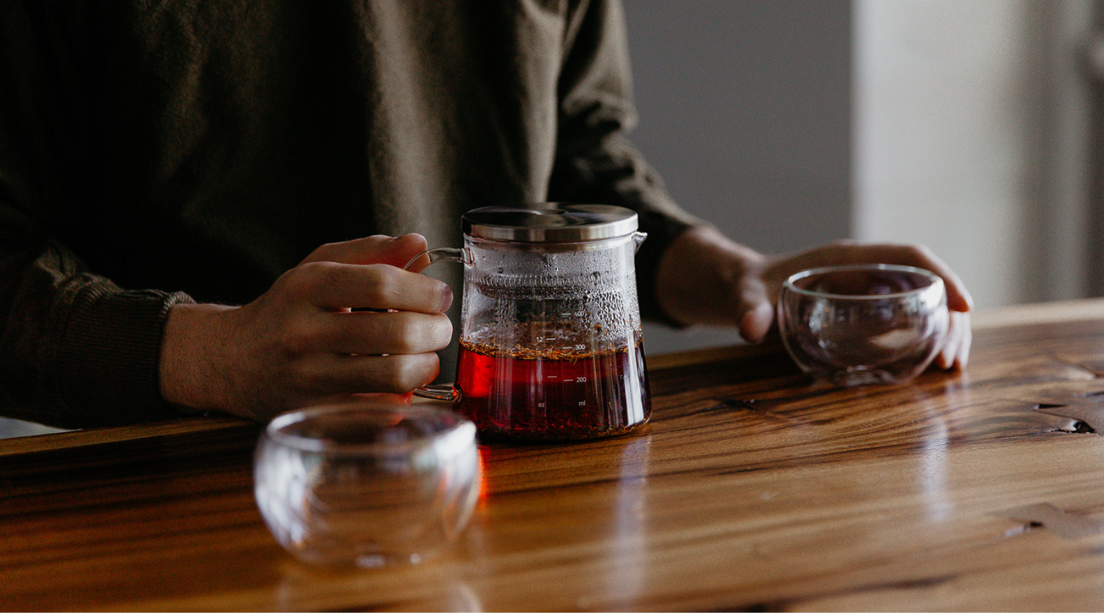 Person holding a glass mug with a wooden table and blurred background