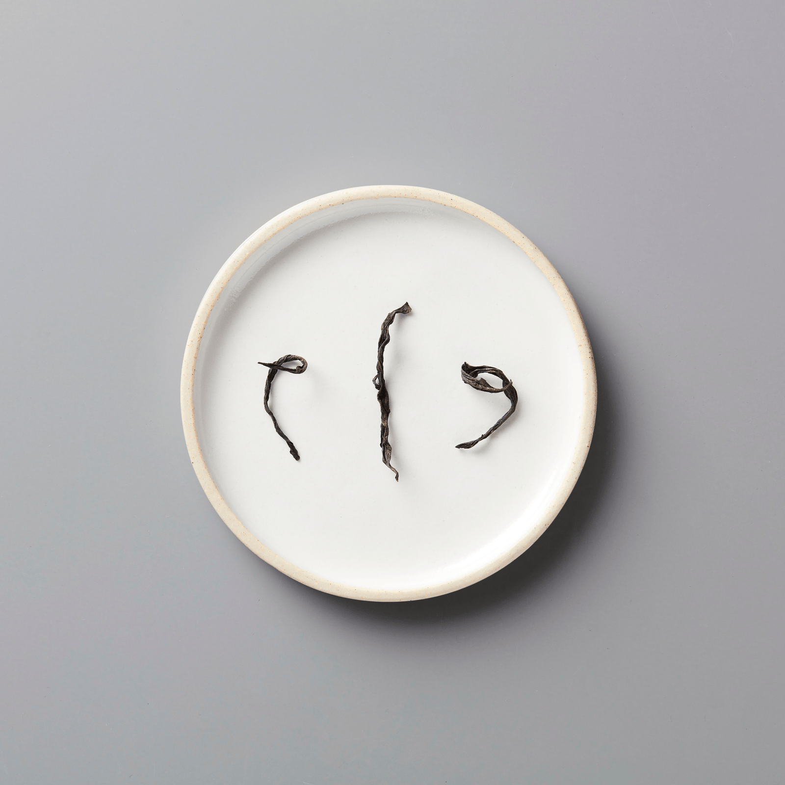 PANLAN 105 yancha oolong tea leaves displayed on white ceramic plate, showing twisted dark strands against plain background