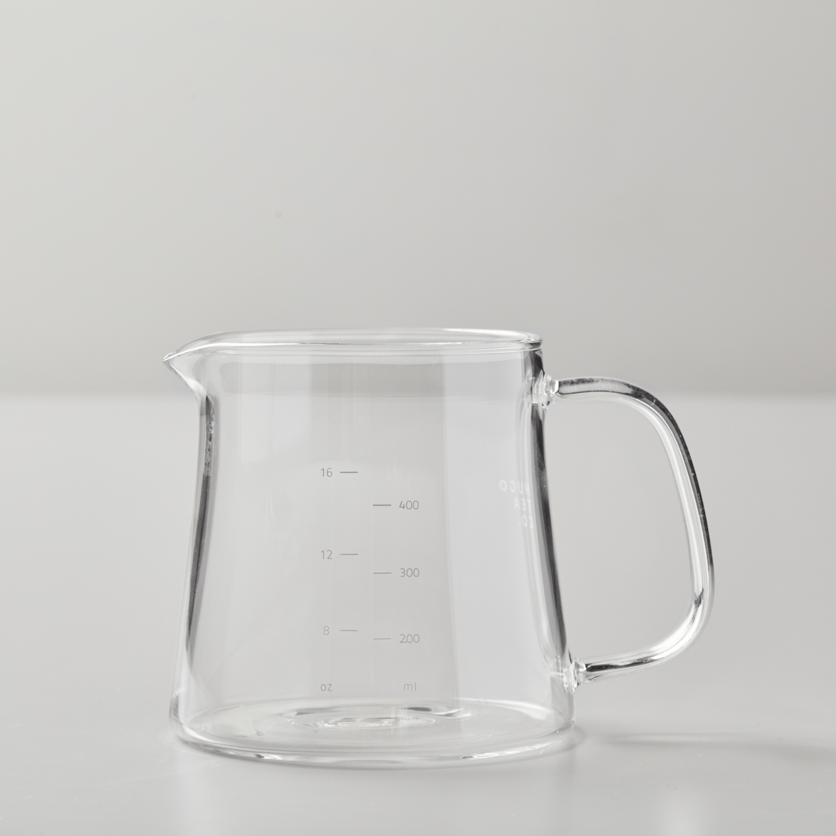 BOLI glass teapot with measurement markings, wide base, and ergonomic handle on minimalist gray background