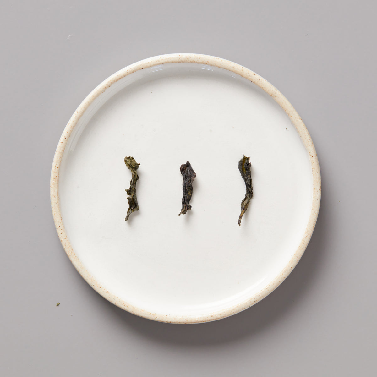 Three twisted Panlan Bei Dou unroasted oolong tea leaves arranged on a round white ceramic plate