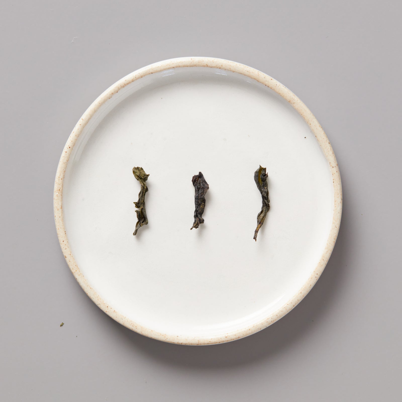 Three twisted Panlan Bei Dou unroasted oolong tea leaves arranged on a round white ceramic plate
