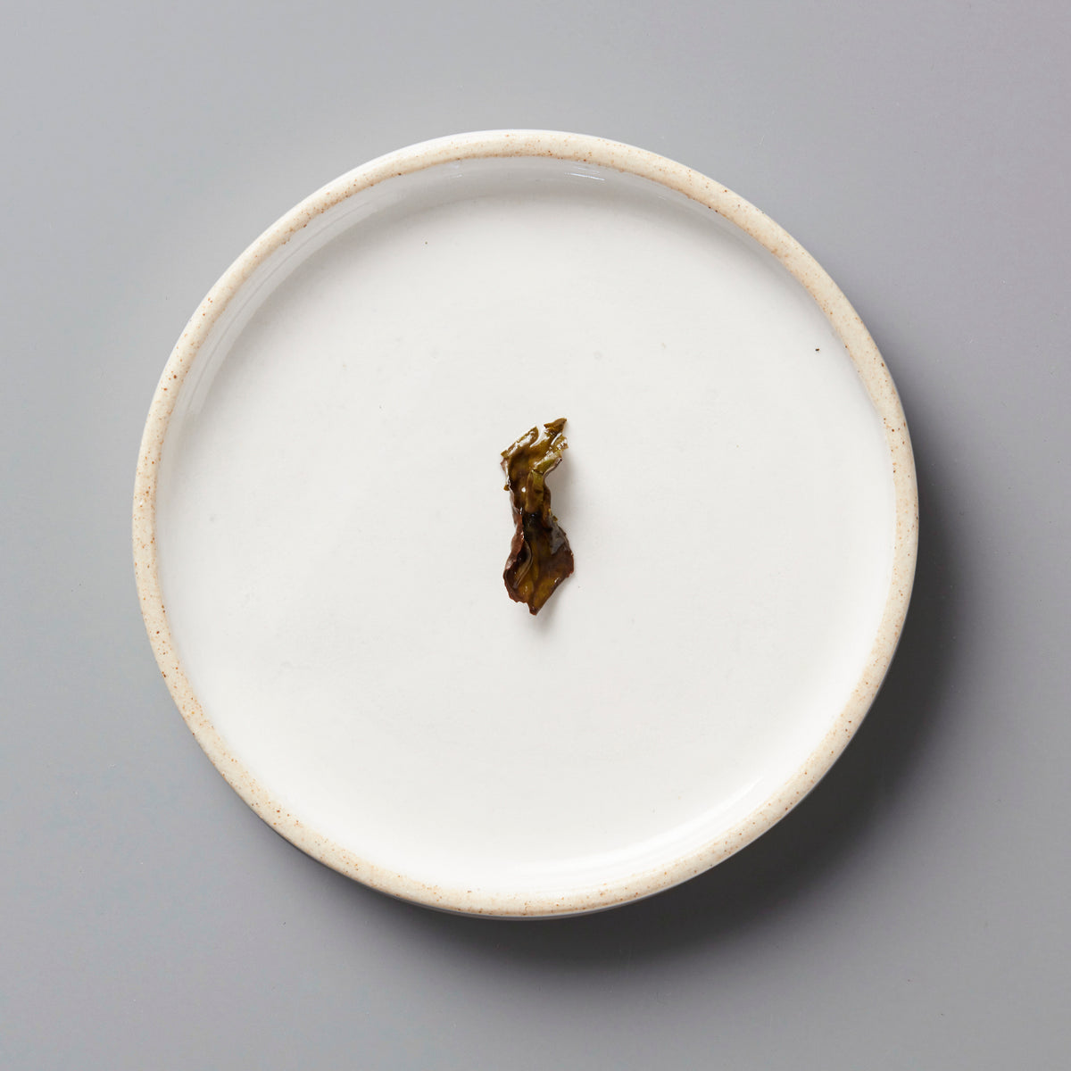 Panlan Bei Dou unroasted oolong tea leaf displayed on a minimalist white ceramic plate against grey background