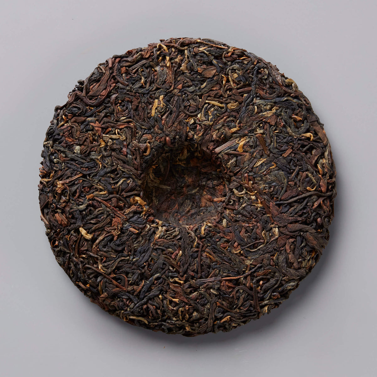 2020 BRUISER black tea cake, compressed dark leaves in traditional circular disc shape against grey background