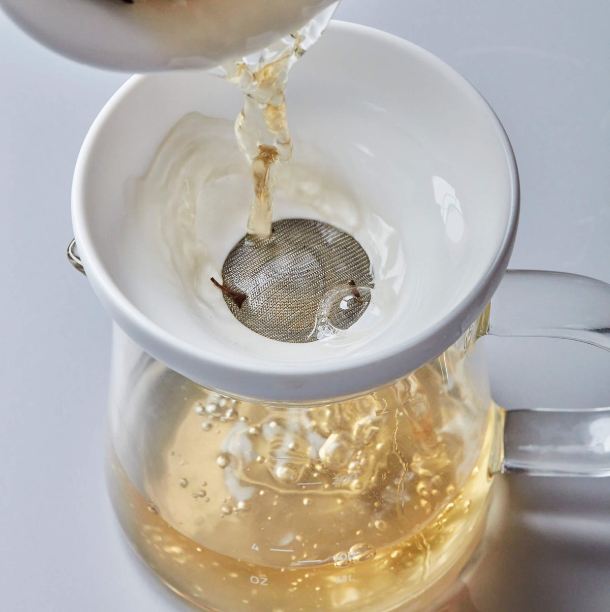 BOLI MINI 200ml glass pitcher with strainer, pouring golden tea through filter into clear vessel